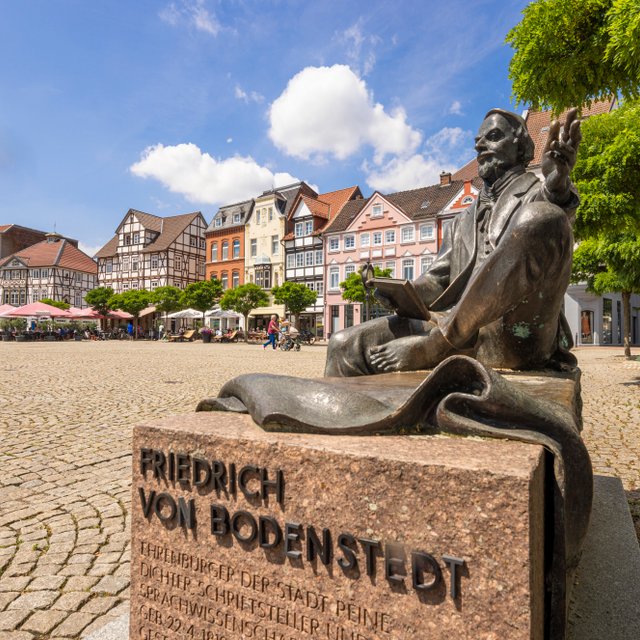 Das Bild zeigt die sitzende Skulptur des Friedrich von Bodenstedt auf dem Historischen Marktplatz in Peine. 