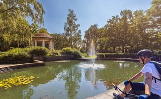 Das Bild zeigt einen Jungen auf einem Fahrrad am Teich im Stadtpark Peine. 