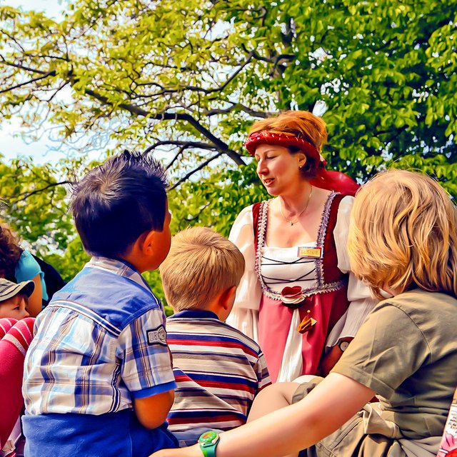 Das Bild zeigt eine Gruppe Kinder, denen die Peiner Burgdame bei einer Kinderstadtführung etwas über Peine erzählt. 