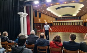 Das Bild zeigt eine Gruppe von Menschen sitzend auf der Bühne des Stadttheaters mit Blick auf den Zuschauersaal.