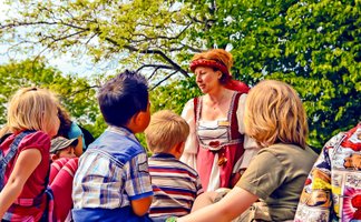 Das Bild zeigt eine Gruppe Kinder, denen die Peiner Burgdame bei einer Kinderstadtführung etwas über Peine erzählt. 