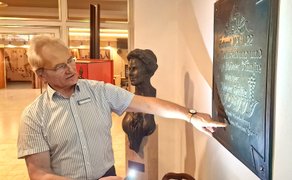 Das Bild zeigt Bühnenmeister Manfred Kubsda, der auf eine Wandtafel im Foyer des Stadttheaters Peiner Festsäle zeigt. 