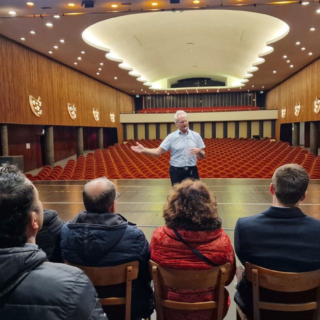 Das Bild zeigt eine Gruppe von Menschen sitzend auf der Bühne des Stadttheaters mit Blick auf den Zuschauersaal.